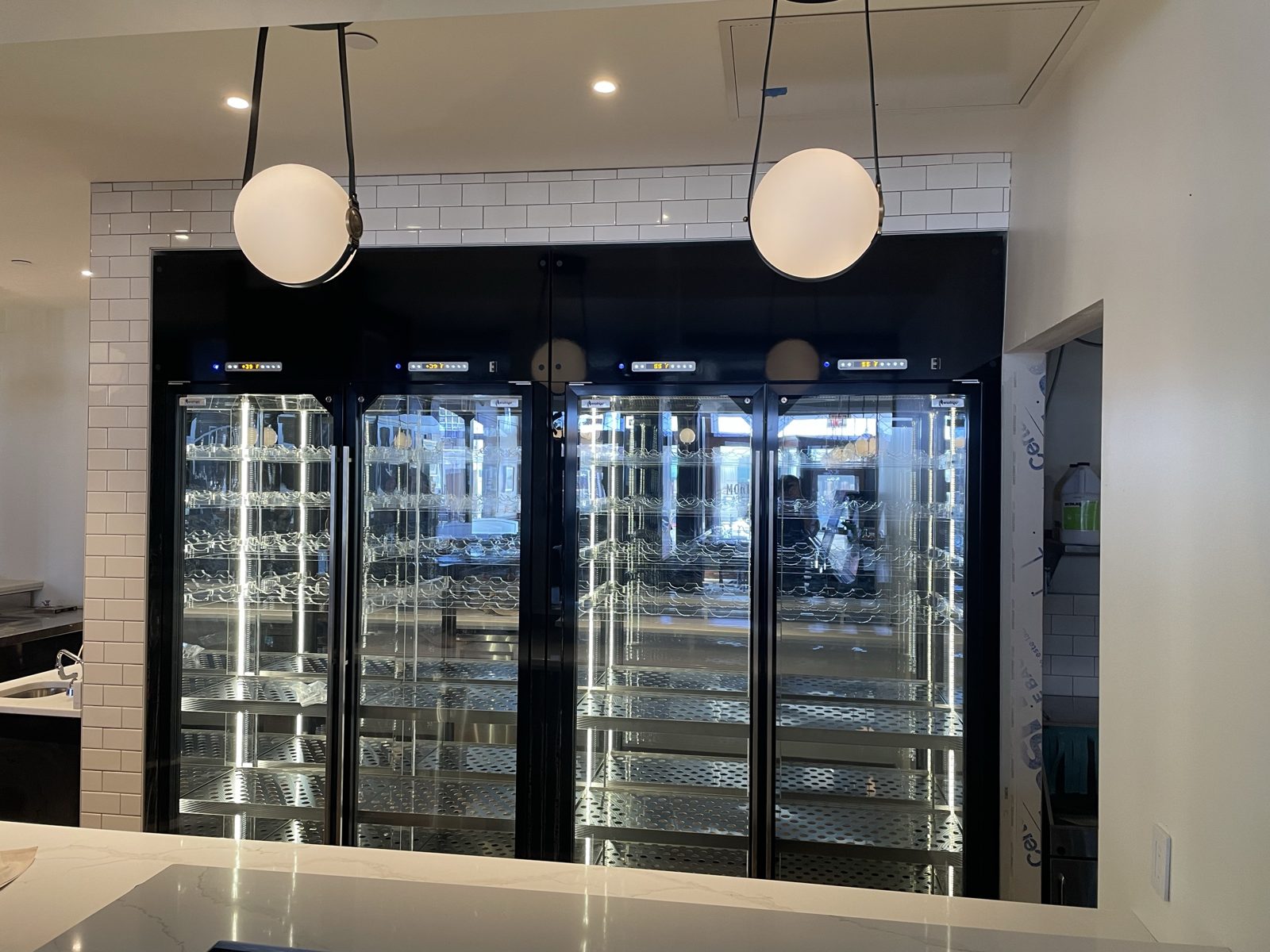 Glass-door wine coolers lit along a hotel bar wall